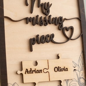 May include: Wooden sign with the text "My missing piece" and a heart shape. Two puzzle pieces are attached to the sign, one with the name "Adrian" and the other with the name "Olivia".