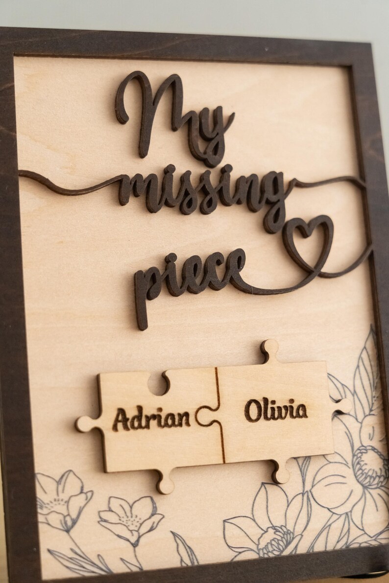 May include: Wooden sign with the text "My missing piece" and a heart shape. Two puzzle pieces are attached to the sign, one with the name "Adrian" and the other with the name "Olivia".
