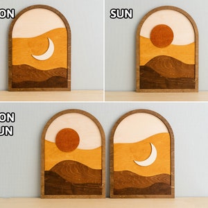 Pu&ograve; includere: Arte da parete in legno con un design paesaggistico minimalista, con un sole o una luna. L'opera d'arte &egrave; in una cornice ad arco marrone scuro, con sfumature a strati di marrone, beige e crema. Le parole "MOON" e "SUN" sono visibili.