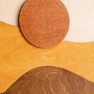 Pu&ograve; includere: Opera d'arte da parete in legno con un design paesaggistico a strati. L'opera incorpora un sole circolare e colline ondulate in tonalit&agrave; di marrone, beige e giallo. Il pezzo &egrave; realizzato in legno e ha una finitura naturale.