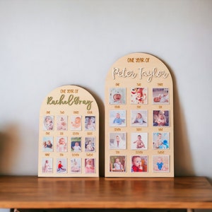May include: Two wooden photo display boards with arched tops. Each board has 12 square spaces for photos and the text "ONE YEAR OF" followed by a name. The name on the left board is "Rachel Gray" and the name on the right board is "Peter Taylor".