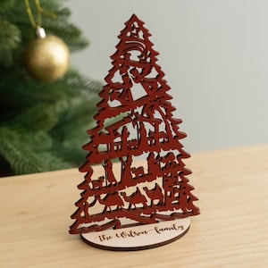 May include: Red wooden Christmas tree ornament with a nativity scene cutout. The base of the tree is personalized with the text "The Wilson Family".
