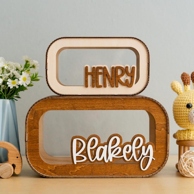 May include: Two wooden name plaques with rounded edges. The top plaque is light wood with the name "HENRY" in dark wood letters. The bottom plaque is dark wood with the name "Blakely" in white letters.