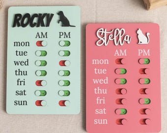 May include: Two pet schedule boards, one mint green and one pink. The mint green board has the name "Rocky" and a dog silhouette. The pink board has the name "Stella" and a cat silhouette. Each board has a weekly schedule with AM and PM toggles.
