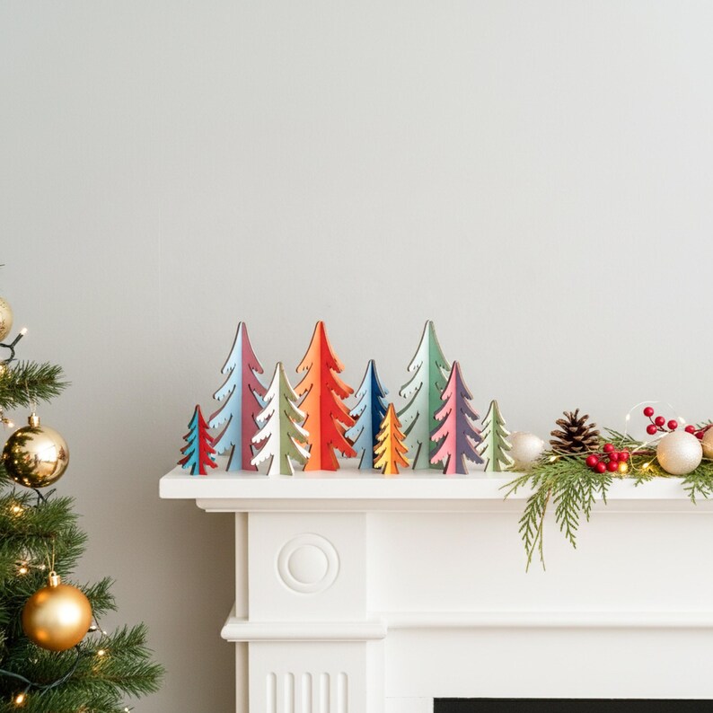 May include: A collection of small, flat, wooden Christmas tree ornaments in various colours including red, blue, orange, green, and purple. The trees are arranged in a row on a white mantelpiece, featuring a mix of solid colours and layered designs.