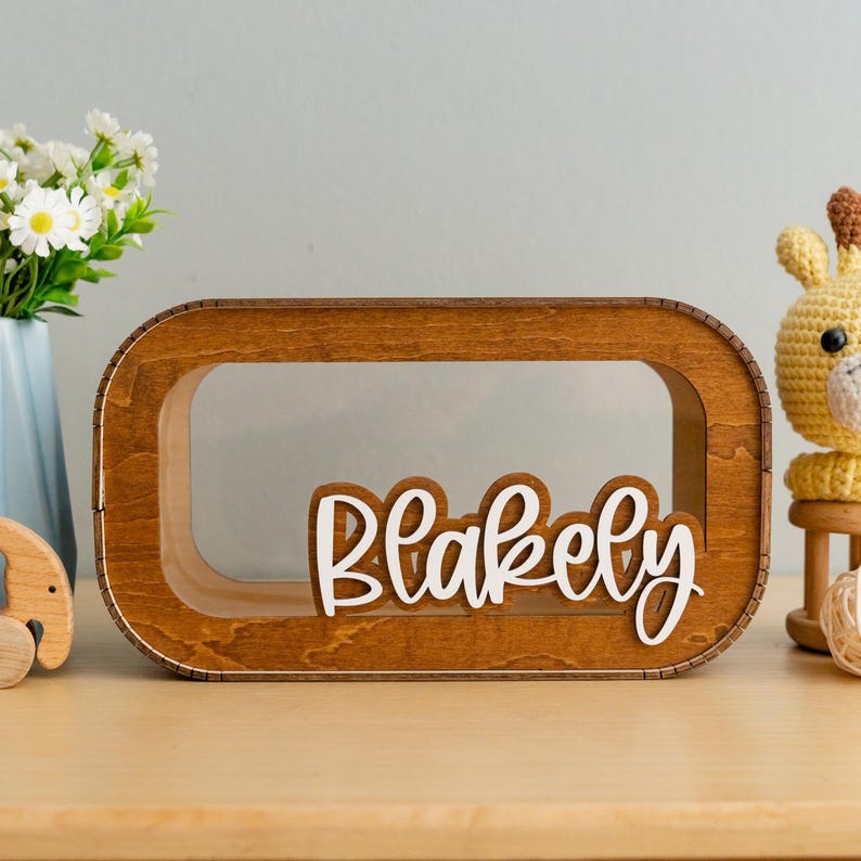 May include: A wooden box with a clear window and the name "Blakely" written in white letters. The box is sitting on a wooden surface.
