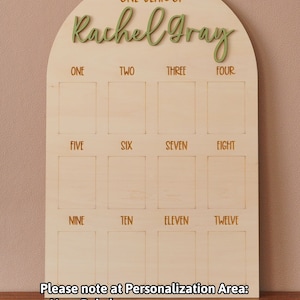 May include: A wooden arch-shaped board with the text "ONE YEAR OF Rachel Gray" at the top. The board has 12 empty squares labeled with the numbers one through twelve. The text "Please note at Personalization Area: + Your Baby's name + Font of the name" is at the bottom.