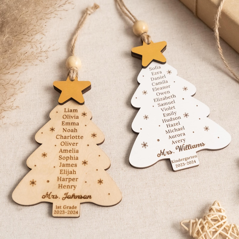 May include: Two wooden Christmas tree ornaments with student names and teacher names. The top ornament is white with the teacher's name "Mrs. Williams" and the grade "Kindergarten" and the year "2023-2024". The bottom ornament is brown with the teacher's name "Mrs. Johnson" and the grade "1st Grade" and the year "2023-2024".