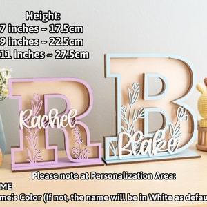 May include: Two wooden letters, R and B, painted in light pink and light blue, with the names Rachel and Blake cut out in white. The letters are decorated with floral designs and stand on a wooden surface. The letters are available in three sizes: 7 inches (17.5 cm), 9 inches (22.5 cm), and 11 inches (27.5 cm).