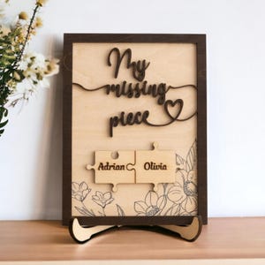 May include: A wooden sign with the text "My missing piece" and a heart shape. Two puzzle pieces with the names "Adrian" and "Olivia" are attached to the sign.