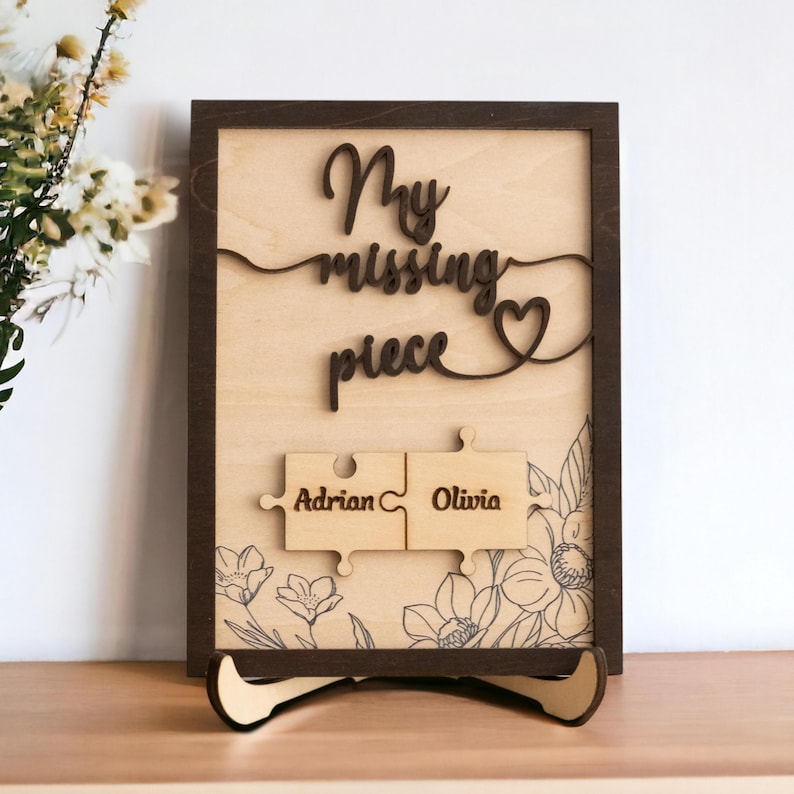 May include: A wooden sign with the text "My missing piece" and a heart shape. Two puzzle pieces with the names "Adrian" and "Olivia" are attached to the sign.