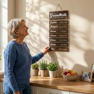 May include: A vertical wooden wall hanging with the text Grandkids make life grand at the top, followed by seven smaller wooden slats connected by metal rings, each featuring a name and a birth date in white script and block lettering.