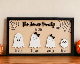 May include: A wooden sign with a black frame featuring a family of ghosts and a cat. The sign reads "The Jones Family Est. 2015" with the names Henry, Olivia, Violet, and Honey below each character.