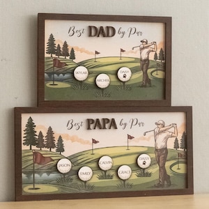 May include: Two framed golf-themed art pieces. The top frame reads "Best DAD by Par" and the bottom frame reads "Best PAPA by Par." Each features a golf course scene with personalized golf balls. The top frame has "Skylar," "Archer," and "Daisy." The bottom frame has "Jason," "Emily," "Calvin," "Grace," and "Daisy."
