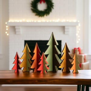 Könnte beinhalten: Eine Sammlung von sieben freistehenden Weihnachtsbaum-Dekorationen aus Holz in verschiedenen Größen. Die Bäume haben ein zweifarbiges Design mit kontrastierenden Farben, darunter Rot-, Orange-, Gelb-, Hellgrün- und Dunkelbrauntöne.