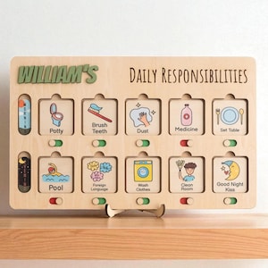 Puede incluir: Tabla de responsabilidades diarias de madera con el nombre "William's" en letras verdes. La tabla incluye ilustraciones para tareas como cepillarse los dientes, poner la mesa y lavar la ropa. Las palabras "Daily Responsibilities" están impresas en la parte superior.