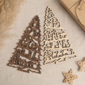 May include: Two wooden Christmas tree ornaments with a nativity scene design. The tree on the left is brown and the tree on the right is natural wood.