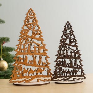 May include: Two wooden Christmas tree ornaments with a nativity scene cutout design. The larger tree is light brown and the smaller tree is dark brown. Both trees have a star at the top and a base.