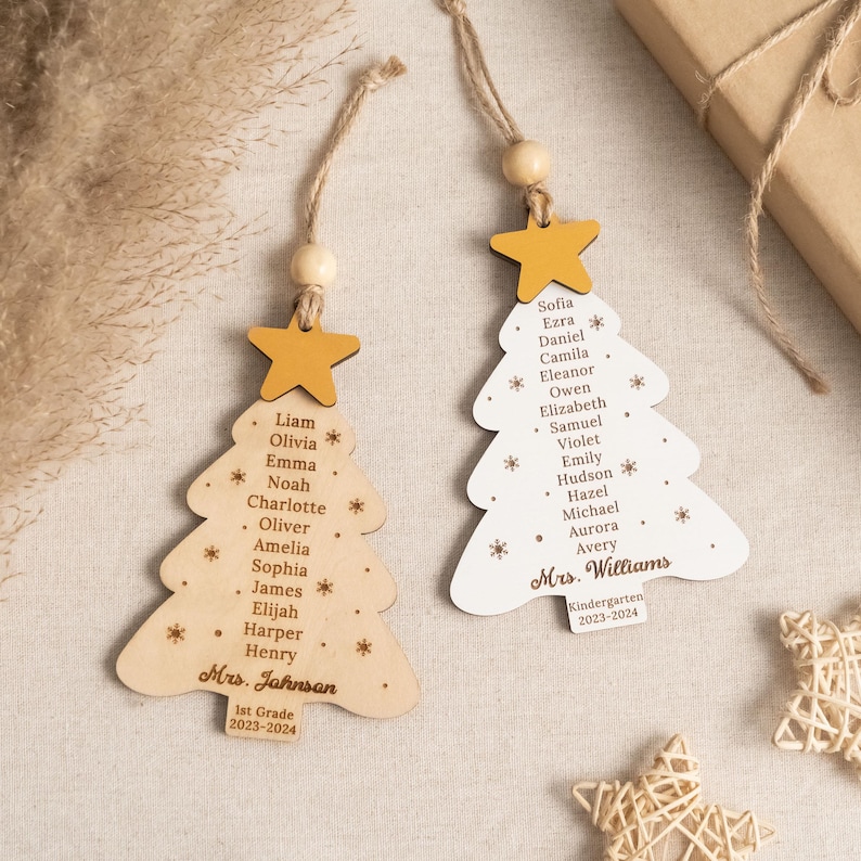 May include: Two wooden Christmas tree ornaments with student names and teacher names. The ornaments are decorated with a yellow star and snowflakes. The text on the ornaments reads "Mrs. Johnsan 1st Grade 2023-2024" and "Mrs. Williams Kindergarten 2023-2024".