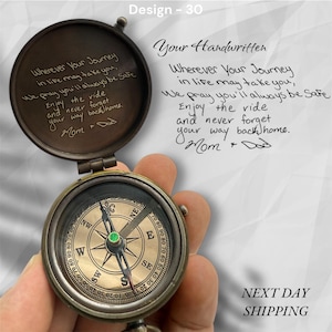 May include: A vintage-style brass compass with a hinged lid, featuring engraved text inside and on the lid. The compass face displays directional markings. The text reads "Wherever Your Journey..." and "Mom + Dad".