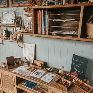Pu&ograve; includere: Un tavolo di legno con una variet&agrave; di materiali naturali, tra cui legno, foglie e pietre. Ci sono anche diversi vassoi con piccoli oggetti, come ghiande, pigne e piume. Il tavolo &egrave; decorato con una lavagna che dice "Riesci a fare queste?"