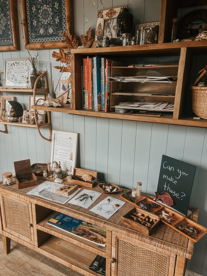 Pu&ograve; includere: Un tavolo di legno con una variet&agrave; di materiali naturali, tra cui legno, foglie e pietre. Ci sono anche diversi vassoi con piccoli oggetti, come ghiande, pigne e piume. Il tavolo &egrave; decorato con una lavagna che dice "Riesci a fare queste?"
