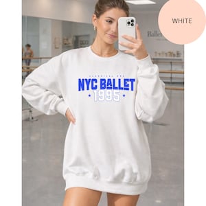 May include: White sweatshirt with the text "NYC BALLET 1995" in blue. The sweatshirt has a crew neck and long sleeves. The text is centered on the front of the sweatshirt. The words "CLASSICAL ERA" are above the text.