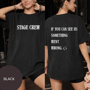 May include: Black t-shirt with the text "STAGE CREW" on the front. The back of the shirt reads "IF YOU CAN SEE US SOMETHING WENT WRONG." with a headphone graphic. The shirt is worn by a person.
