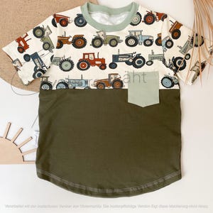 Könnte beinhalten: Ein weißes T-Shirt mit kurzen Ärmeln und einer grünen und braunen Tasche auf der Vorderseite. Das Shirt hat ein Muster aus Comic-Traktoren in verschiedenen Farben auf der oberen Hälfte.