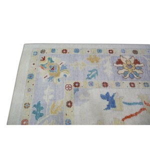 Pode incluir: Um tapete vintage com fundo azul claro e um padr&atilde;o floral em tons de amarelo, laranja, vermelho e azul. O tapete tem uma borda com um padr&atilde;o repetitivo de pequenas flores.