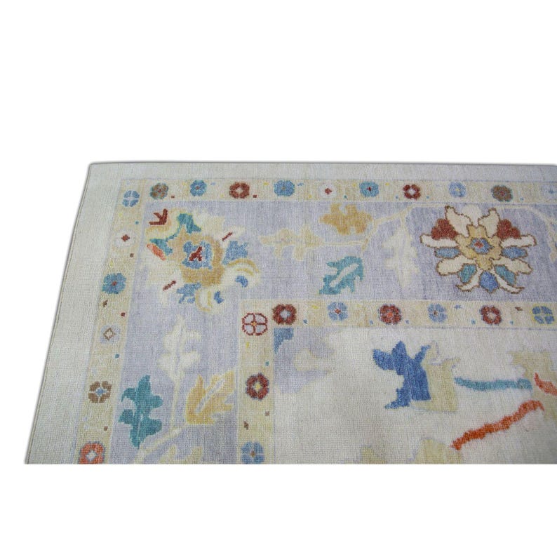 Pode incluir: Um tapete vintage com fundo azul claro e um padr&atilde;o floral em tons de amarelo, laranja, vermelho e azul. O tapete tem uma borda com um padr&atilde;o repetitivo de pequenas flores.
