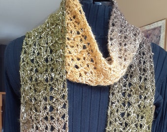 May include: A crocheted scarf in shades of brown, gold, and green. The scarf is made with a lacy stitch pattern and has a gradient of colour.