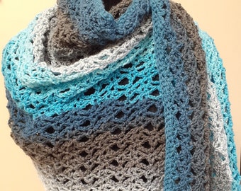 May include: A crocheted shawl in shades of blue, grey, and white. The shawl is made with a lacy stitch and has a fringed edge.