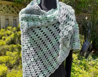 May include: A crocheted shawl in shades of green and grey, draped over a mannequin. The shawl has a lacy, openwork design.