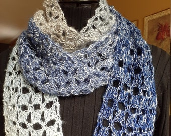 May include: A crocheted scarf with a gradient of blue and grey colours. The scarf is made with a delicate open stitch pattern.