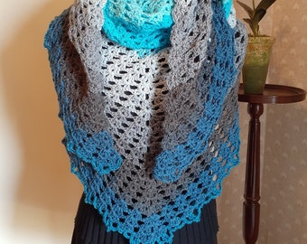 May include: A crocheted shawl in shades of blue and grey with a delicate lace pattern. The shawl is draped over a dress form and is ready to be worn.