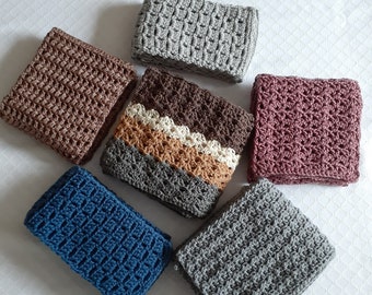 May include: Seven crocheted headbands are arranged in a circular pattern. The headbands are in shades of brown, grey, blue, and pink. The crochet patterns vary, with some featuring textured designs and others a more open weave.