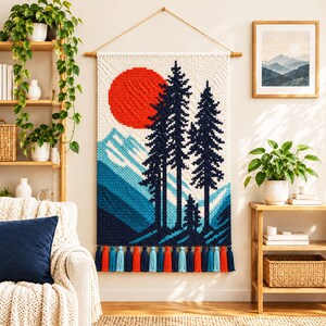 May include: A rectangular macrame wall hanging featuring a landscape design with a large red sun, dark blue pine trees, and blue mountain peaks. The piece is suspended from a wooden rod with a rope and finished with a row of colorful tassels.