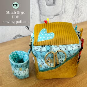 Puede incluir: Un kit de costura amarillo mostaza y verde azulado con un aplique en forma de corazón y un diseño de cinta métrica. El kit incluye una taza pequeña, tijeras y el texto "Stitch & go PDF sewing pattern."