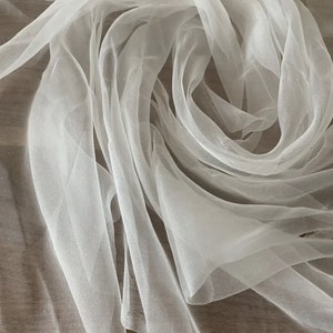 May include: White sheer fabric with a soft, delicate texture. The fabric is draped and folded, creating a flowing and ethereal look.