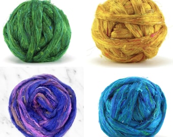 May include: Four colorful yarn balls in green, gold, purple, and blue. The yarn balls are round and appear to be made of a textured fiber. The green ball has blue accents, the gold ball has pink accents, the purple ball has pink and brown accents, and the blue ball has green accents.