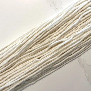May include: A close-up of a bundle of white cotton yarn. The yarn is soft and fluffy, and it is perfect for knitting or crocheting.