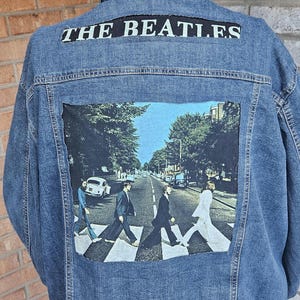 Puede incluir: Chaqueta vaquera azul con un gráfico de la portada del álbum Abbey Road de The Beatles en la espalda. El nombre de la banda está impreso en la parte superior de la espalda. Un clásico de la memorabilia musical.