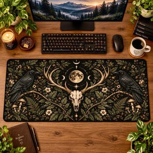 May include: A rectangular desk mat featuring a dark forest illustration with a central deer skull, a full moon, and two ravens perched on branches. The design includes oak leaves, small white flowers, and mushrooms in shades of green, brown, and cream.