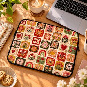 Peut inclure: Une housse d'ordinateur portable rectangulaire présentant un motif en grille répétitif de carreaux carrés colorés. Chaque carreau affiche des illustrations distinctes incluant diverses fleurs, soleils, arcs-en-ciel et cœurs dans des tons de rouge, rose, jaune et vert.