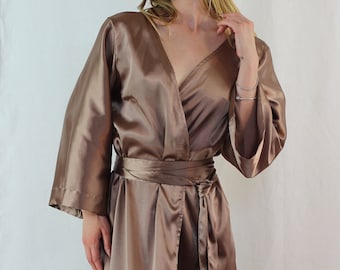 May include: A long, brown satin robe with a wrap style and a tie belt. The robe has long sleeves and a V-neckline.
