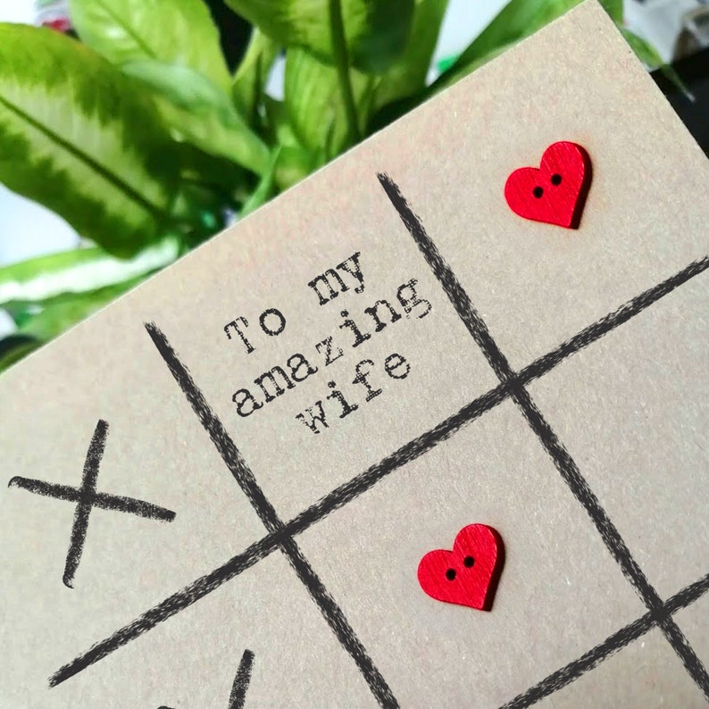 May include: A card with the text "To my amazing wife" and a tic-tac-toe board with red heart buttons.