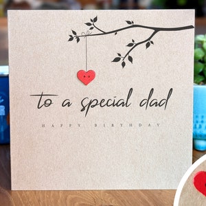 May include: A brown card with a black branch with leaves and a red heart hanging from it. The text on the card reads "to a special dad happy birthday".
