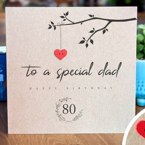 May include: A brown card with a black branch with leaves and a red heart hanging from it. The card says "to a special dad happy birthday 80" in black text.