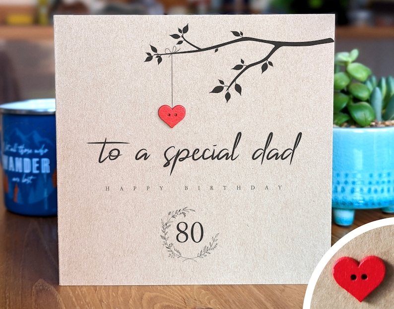 May include: A brown card with a black branch with leaves and a red heart hanging from it. The card says "to a special dad happy birthday 80" in black text.